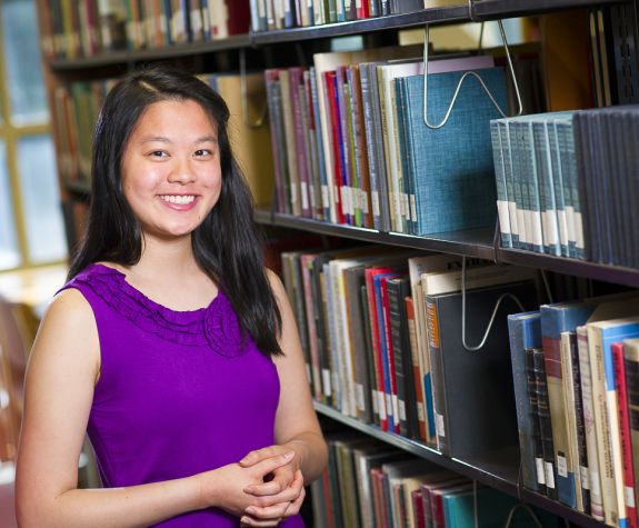Scholarship winner smiles in library stacks.